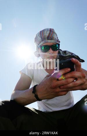 13.07.2021, Allemagne, Mecklembourg-Poméranie occidentale, Wolgast - Jeune homme avec foulard et lunettes de soleil regardant son smartphone. 00S210713D010CAROEX.J. Banque D'Images