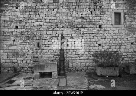 une ancienne fontaine devant un mur de pierre, noir et blanc Banque D'Images