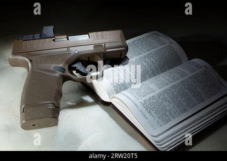 Pistolet semi-automatique brun de 9 mm avec une bible en dessous ouvert sur le passage dans Luc dans lequel Jésus dit à ses disciples d'acheter une épée Banque D'Images