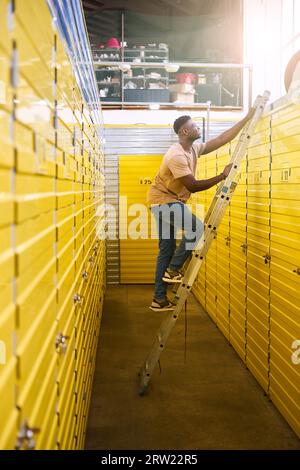 Mec aux cheveux bouclés en Jean se tient sur un escabeau près des conteneurs de stockage Banque D'Images