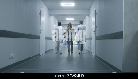 Photo suivante de médecins marchant le long du couloir moderne du centre médical. Les spécialistes de la santé et l'infirmière entrent dans la chambre d'hôpital pour le patient ou le bureau. Le personnel médical dans le couloir de la clinique. Banque D'Images