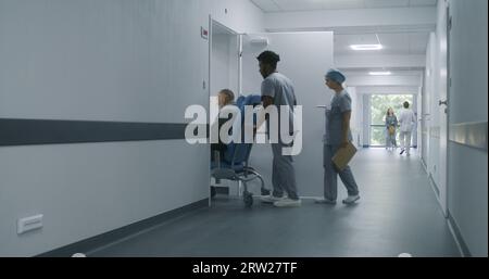 Jeune infirmière ouvre la porte au cabinet médical avec la carte-clé. Un médecin afro-américain transporte un patient âgé dans un cabinet médical. Le médecin féminin marche dans le couloir de l'hôpital avec les résultats des tests médicaux. Banque D'Images