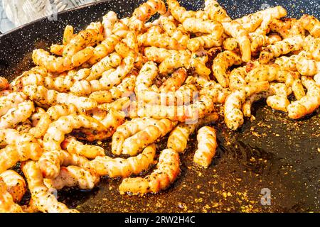De grosses crevettes ont été cuites. Gros plan de beaucoup de crevettes à frire dans une grande poêle avec de l'huile et des herbes à l'extérieur au soleil. Banque D'Images