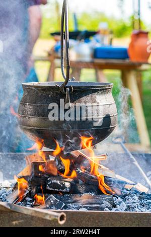 Petit chaudron médiéval rempli d'eau suspendu au-dessus d'un feu de bois coupé lors d'une reconstitution au centre médiéval Sandwich. Banque D'Images