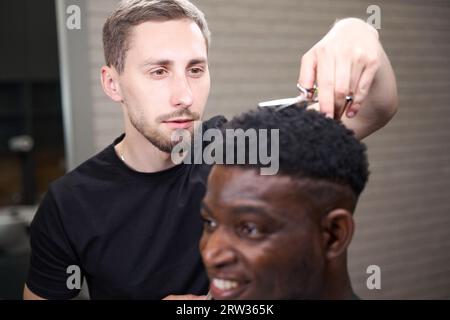 Un client afro-américain se fait couper les cheveux dans un salon de coiffure caucasien Banque D'Images