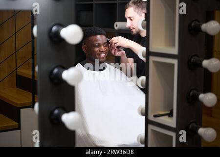 Maître coupe les cheveux des clients devant le miroir dans le salon de coiffure Banque D'Images