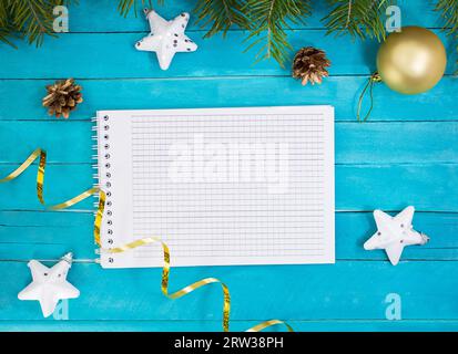 Bloc-notes avec étoiles blanches, serpentine, pommes de pin, boule de Noël et branches d'épicéa sur des planches bleues. Nouvel an Banque D'Images