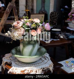 Un bouquet de roses artificielles, hortensias, marguerites dans une cruche en céramique verte à un marché aux puces sur une table. Banque D'Images