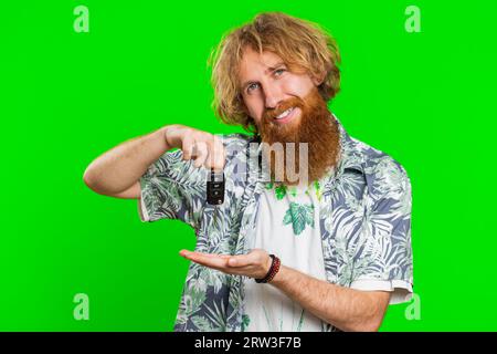 Homme barbu caucasien souriant confiant acheteur montrant la clé de la nouvelle voiture, affaires automobiles, achat de véhicule, vente de succès, location, achat. Heureux excité Redhead gars isolé sur fond vert chroma key Banque D'Images