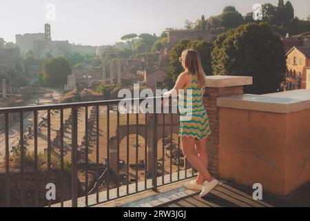 Une jeune touriste blonde profite de la vue sur les anciennes ruines classiques de l'historique Forum romain comme vu de la colline du Capitole ou Campidogl Banque D'Images