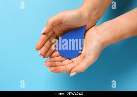 Mains féminines avec goutte de papier sur fond bleu. Journée mondiale de la poliomyélite Banque D'Images