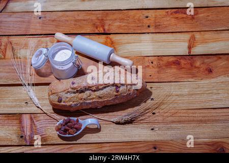 Pain rustique aux raisins sur une table en bois avec de la farine, des chevilles de blé et un rouleau à pâtisserie Banque D'Images