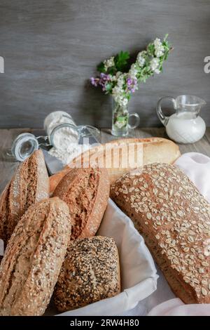 Miches et miches de pain artisanal rustique fait avec différents types de graines et farines, avec un pot de lait et un pot de farine sur blanc et rose Banque D'Images