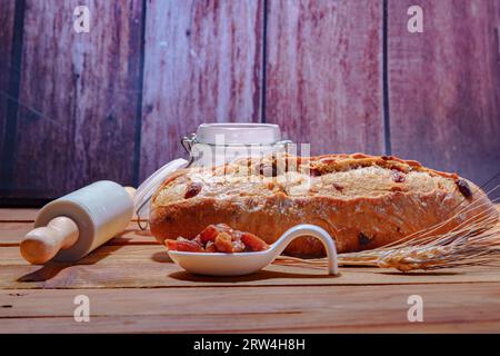 Pain rustique aux raisins sur une table en bois avec de la farine, des chevilles de blé et un rouleau à pâtisserie Banque D'Images