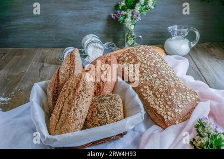 Miches et miches de pain artisanal rustique fait avec différents types de graines et farines, avec un pot de lait et un pot de farine sur blanc et rose Banque D'Images