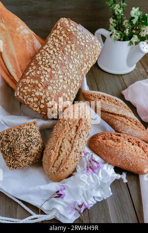 Différents types de pain rustique fait à la main à base de graines sur un tissu rose sur une table en bois décorée de fleurs Banque D'Images