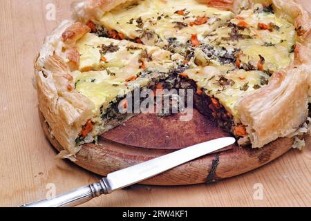 Tarte aux épinards et au saumon sur une assiette en bois. Diagonalement au premier plan un vieux couteau Banque D'Images