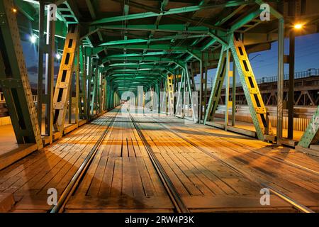 Tramway avec deux voies dans la partie inférieure du pont de Gdanski en treillis d'acier à Varsovie, Pologne, illumination nocturne, perspective de point de fuite Banque D'Images
