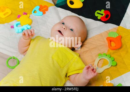 Mignon petit bébé nouveau-né entouré de jouets colorés, allongé à la maison sur le lit Banque D'Images