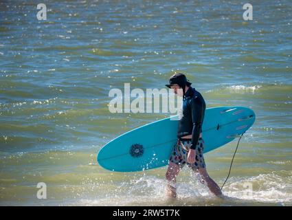 Cape May, États-Unis. 16 septembre 2023. Un surfeur marche avec sa planche tout en partant survoler quelques vagues qui sont des restes de l'ouragan Lee alors que les gens ont apprécié le temps chaud samedi 16 septembre 2023 à Cove Beach à Cape May, New Jersey. Les températures étaient dans le bas des années 80 le dernier week-end avant l'automne. ( Crédit : William Thomas Cain/Alamy Live News Banque D'Images