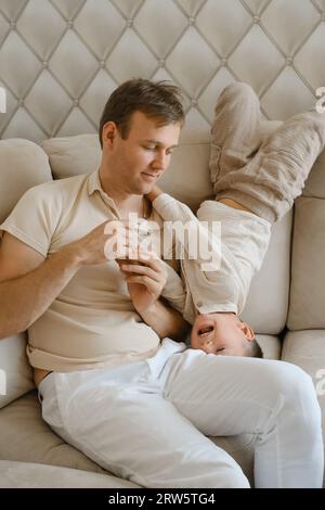 Père jouant avec enfant en bas âge sur le canapé. Parent s'amusant avec le garçon en bas âge. Temps de famille et parentalité. Papa passant du temps avec son fils Banque D'Images