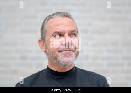 Gros plan portrait d'un homme sérieux attrayant regardant sur le côté devant un mur de briques blanches Banque D'Images