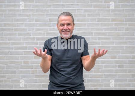 Portrait du haut du corps d'un homme amical attrayant montrant avec un geste, que dois-je faire, ce que tu veux de moi, devant un mur de briques blanches Banque D'Images