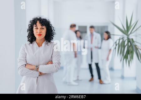 Médecin femme confiante en uniforme médical debout à l'intérieur, bras pliés. Heureux et satisfait, en regardant la caméra. Banque D'Images