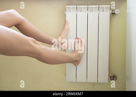 Une femme chauffe ses pieds sur un radiateur à la maison, maison chaude, saison de chauffage, réchauffe ses pieds en hiver sur un radiateur en Ukraine Banque D'Images