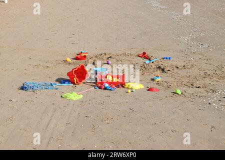 Une gamme de jouets colorés et amusants sont dispersés sur la plage de sable, offrant une atmosphère amusante et ludique Banque D'Images