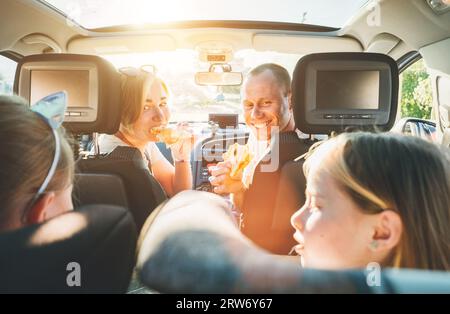 Jeune couple avec des filles mangeant une pizza italienne juste cuite dans une voiture moderne avec toit transparent. Des moments de famille heureux, l'enfance, la restauration rapide e Banque D'Images