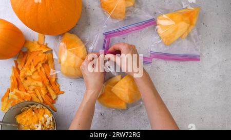 Des tranches de citrouille fraîches, brutes et pelées dans des sacs à fermeture à glissière, prêtes à être congelées.Femme mains, plat Banque D'Images