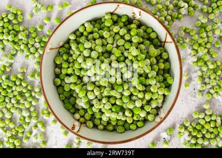 Pois verts congelés dans un bol en gros plan d'en haut sur fond gris clair Banque D'Images