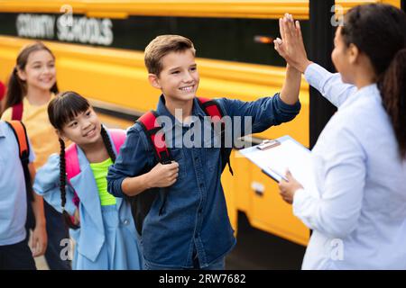 Enseignante féminine noire donnant High Five au garçon entrant dans le bus scolaire Banque D'Images