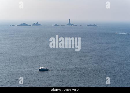 Bateau de pêche passant devant le phare de Longships et les îlots rocheux au large de la côte des Cornouailles Banque D'Images
