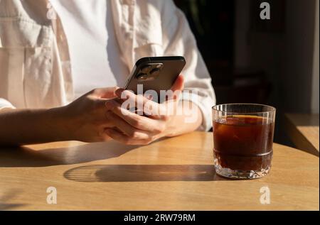 Berlin, Allemagne septembre 16 2023 mains tenant le téléphone portable, en utilisant smartphone à la table en bois dans le café, café Banque D'Images