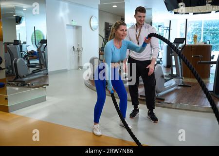 Femme persistante utilisant des cordes de combat pour l'entraînement intense de renforcement de la force Banque D'Images