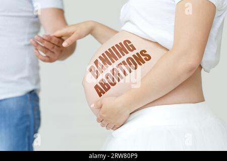 Une femme enceinte tient la main de son mari sur son ventre avec l'inscription - INTERDICTION DES AVORTEMENTS. Concept de grossesse. Banque D'Images