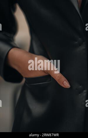 Main féminine dans la poche. Détails de mode d'une veste en cuir noir. Tenue fantaisie, prise de vue verticale Banque D'Images