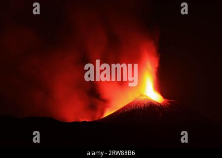 Etna dans une éruption de lave nocturne avec cratère de silhouette rétro-éclairé et de grandes émissions de fumée dans une vue panoramique du volcan sicile Banque D'Images