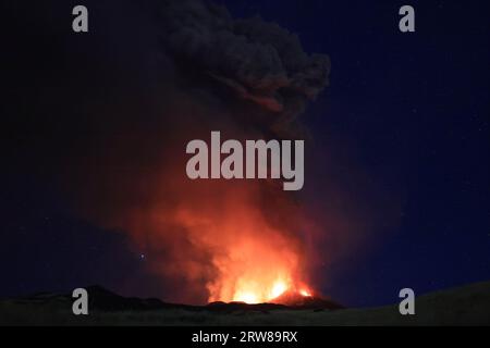 Éruption de l’Etna en Sicile avec vue panoramique sur la grande colonne de fumée et de cendres du cratère du volcan dans le ciel étoilé nocturne d’août 2023 Banque D'Images