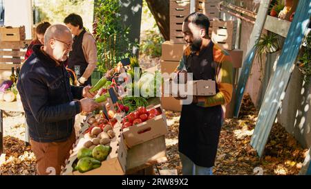 Agriculteur afro-américain vendant des produits maison à un vieux client, parlant de fruits et légumes frais naturels. Vendeur masculin présentant ses produits biologiques du jardin personnel. Banque D'Images