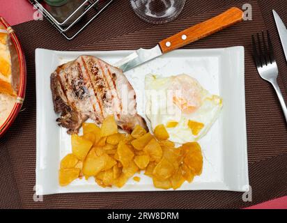 Deux côtelettes de porc frites avec os, complétées par des tranches de frites, un œuf au plat et du pain au son Banque D'Images