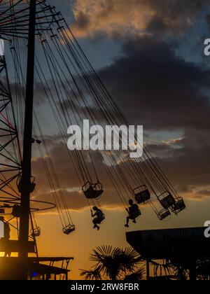 Silhouettes de personnes sur le carrousel. Concept de plaisir et de divertissement. Les gens sur les carrousels au coucher du soleil. Station balnéaire. Lunapark. Adrénaline. Carous de vitesse Banque D'Images