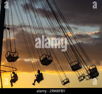 Silhouettes de personnes sur le carrousel. Concept de plaisir et de divertissement. Les gens sur les carrousels au coucher du soleil. Station balnéaire. Lunapark. Adrénaline. Carous de vitesse Banque D'Images