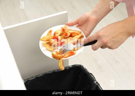 Femme jetant des pommes de terre cuites avec du ketchup dans la poubelle à l'intérieur, gros plan Banque D'Images