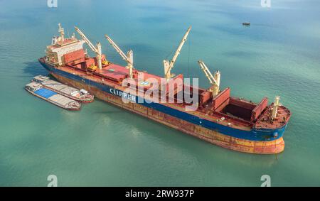 Le vraquier Clipper Kythira ancré dans la baie d'Halong (Hạ long), Vietnam, déchargeant la cargaison dans des barges de fret locales parmi les falaises de calcaire touristiques Banque D'Images