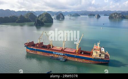 Le vraquier Clipper Kythira ancré dans la baie d'Halong (Hạ long), Vietnam, déchargeant la cargaison dans des barges de fret locales parmi les falaises de calcaire touristiques Banque D'Images