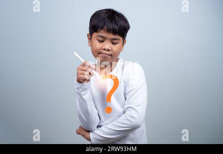 Un garçon en chemise blanche tient un stylo blanc sur fond blanc. Fait preuve de réflexion, de réflexion et d'examen des options. Banque D'Images