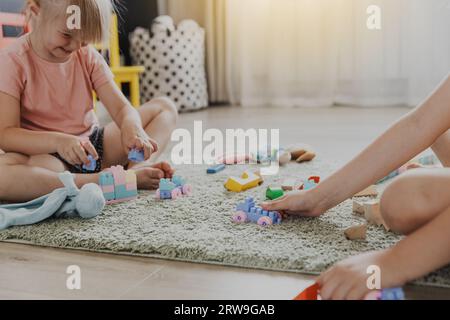 Enfants jouant avec le train coloré de jouet en plastique coloré. Les enfants assis sur le tapis à l'intérieur à la chambre à coucher blanche ensoleillée à la maison ou à la maternelle, garderie. Marrant Banque D'Images